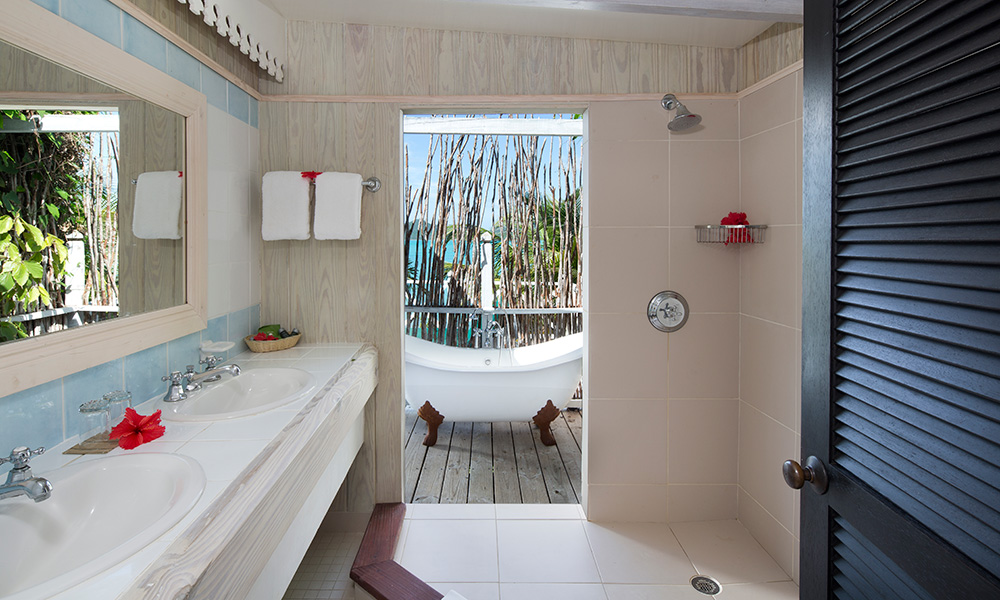 Bathroom with double vanity and walk-in shower opening to an outdoor soaking tub overlooking the ocean at Cocobay Resort Antigua.
