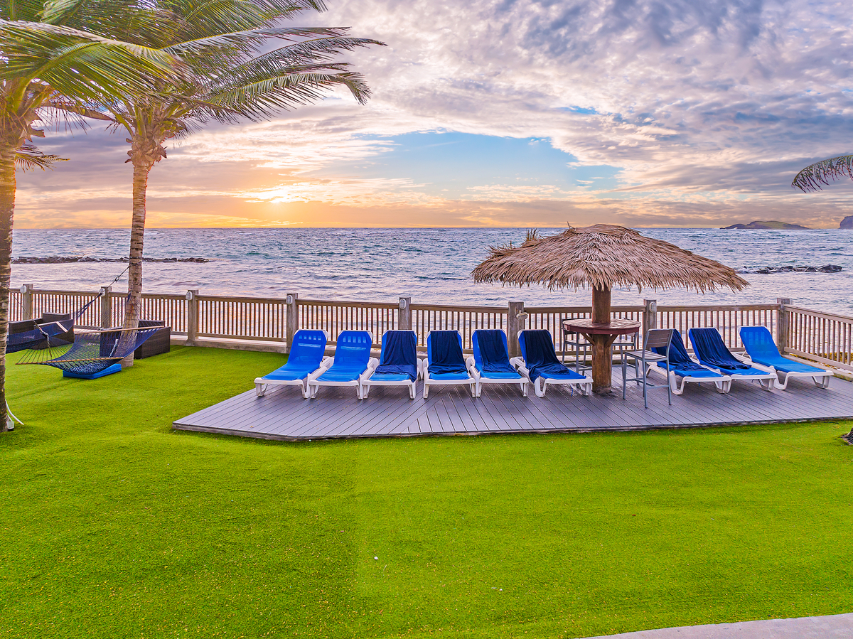 Blue loungers arranged on a wooden deck overlooking the ocean at Coconut Bay Beach Resort & Spa, with palm trees and a thatched umbrella nearby.
