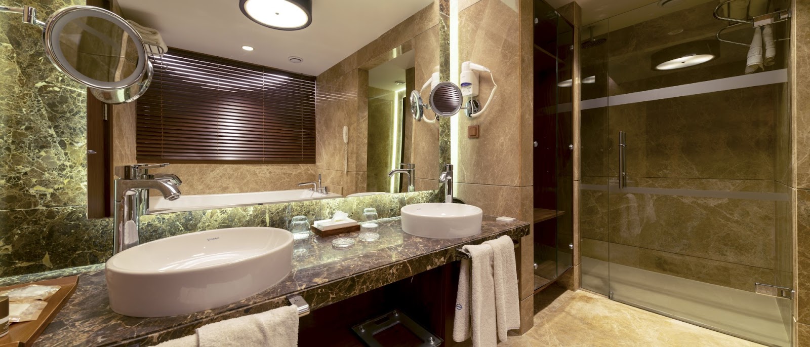Luxury bathroom with dual vessel sinks, marble countertop, glass shower enclosure, and illuminated mirrors at Concorde De Luxe Resort.