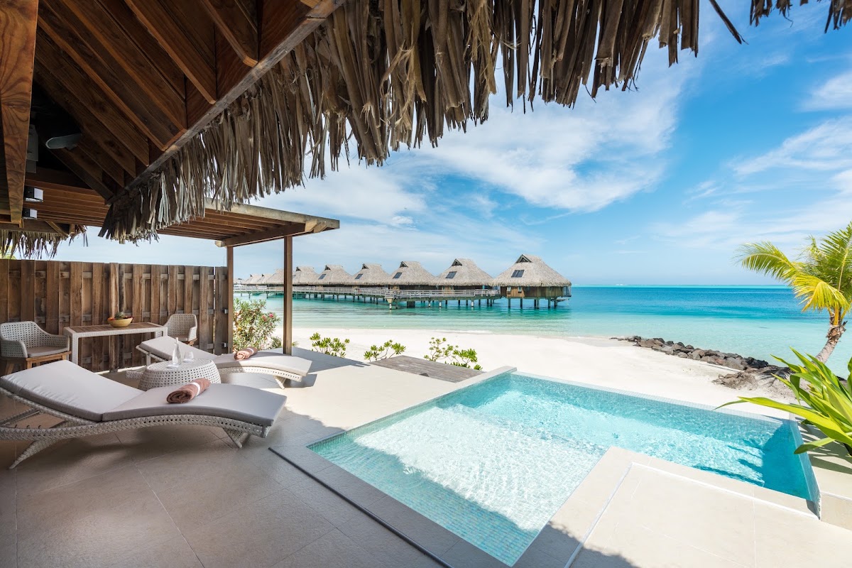 Conrad Bora Bora Nui villa with private pool, loungers, and thatched-roof overwater bungalows beyond turquoise lagoon.
