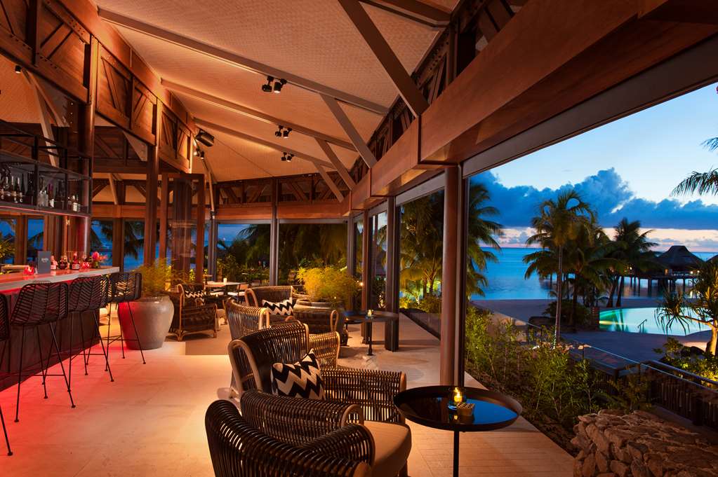 Open-air lounge at Conrad Bora Bora Nui with woven chairs, bar seating, and views of the lagoon and overwater bungalows at sunset.