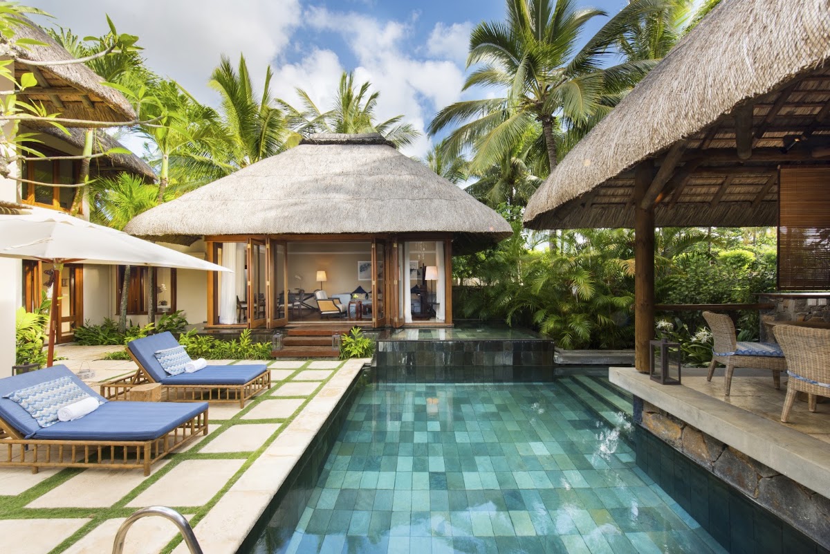 Thatched-roof villa with private pool at Constance Belle Mare Plage, surrounded by loungers and palm trees.