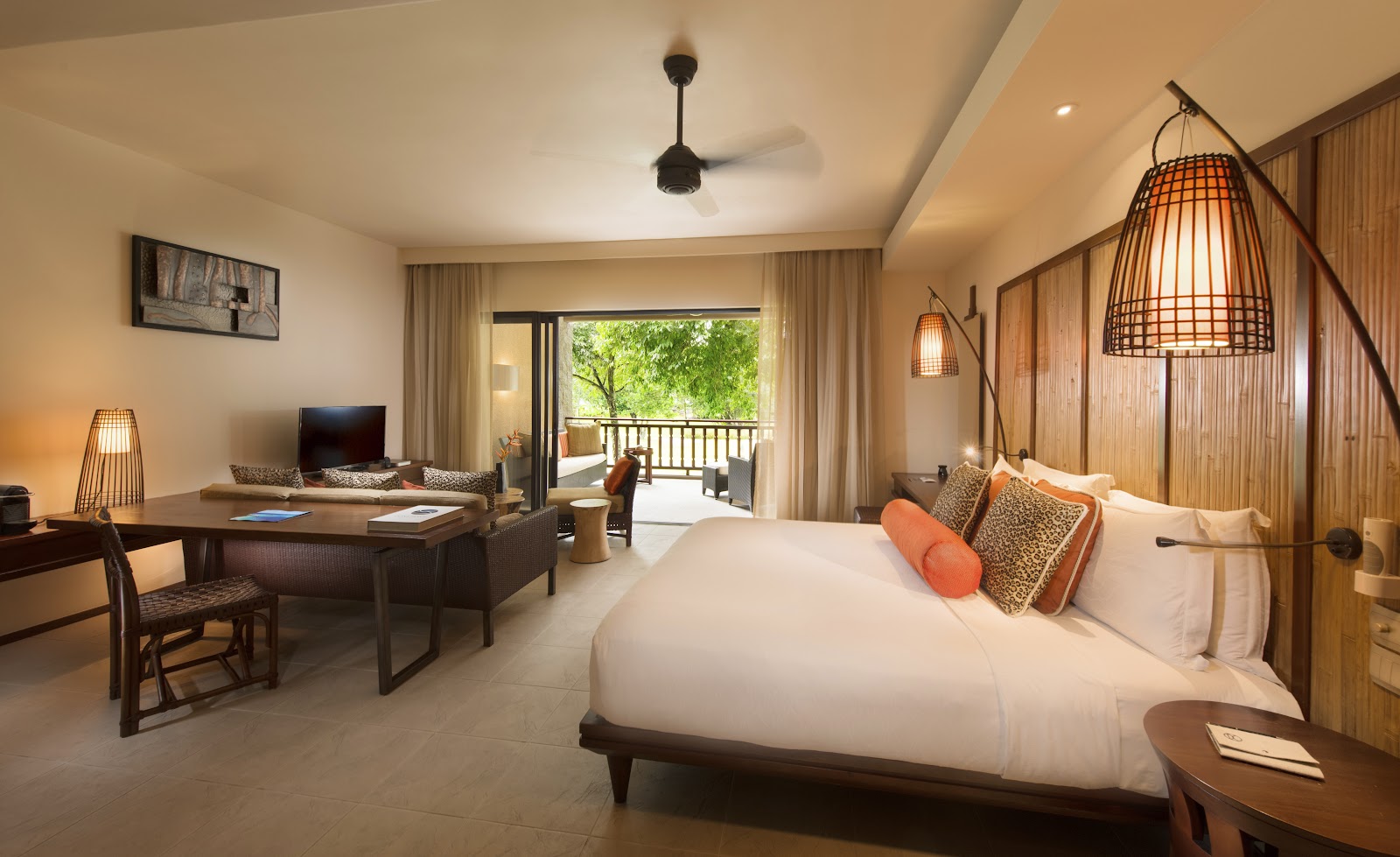 Spacious resort suite with king bed, seating area, desk, and balcony overlooking tropical greenery at Constance Ephelia.