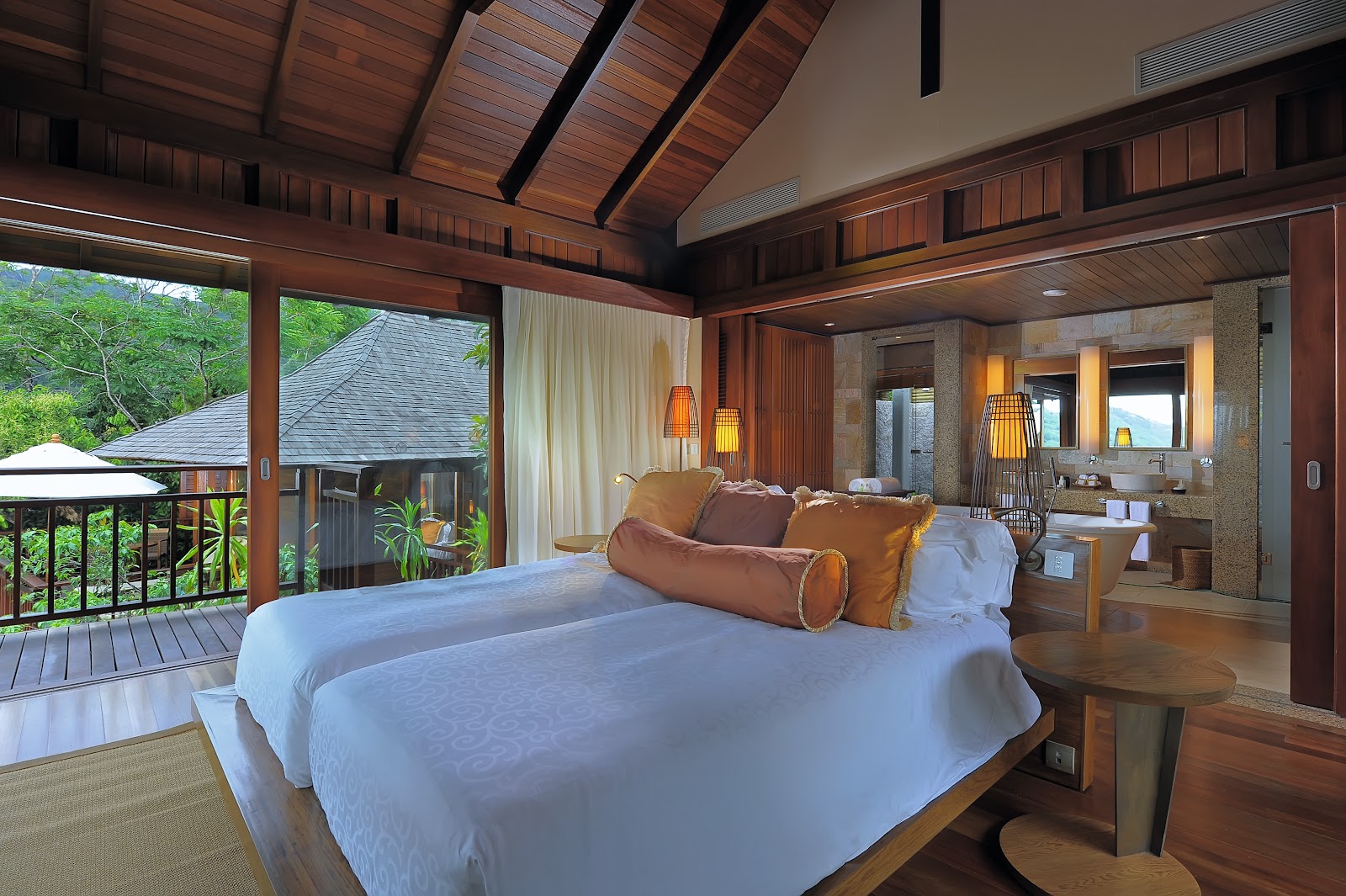 Infinity pool reflects illuminated villa interiors and warm accent lighting at dusk, with open-air living spaces visible beyond.