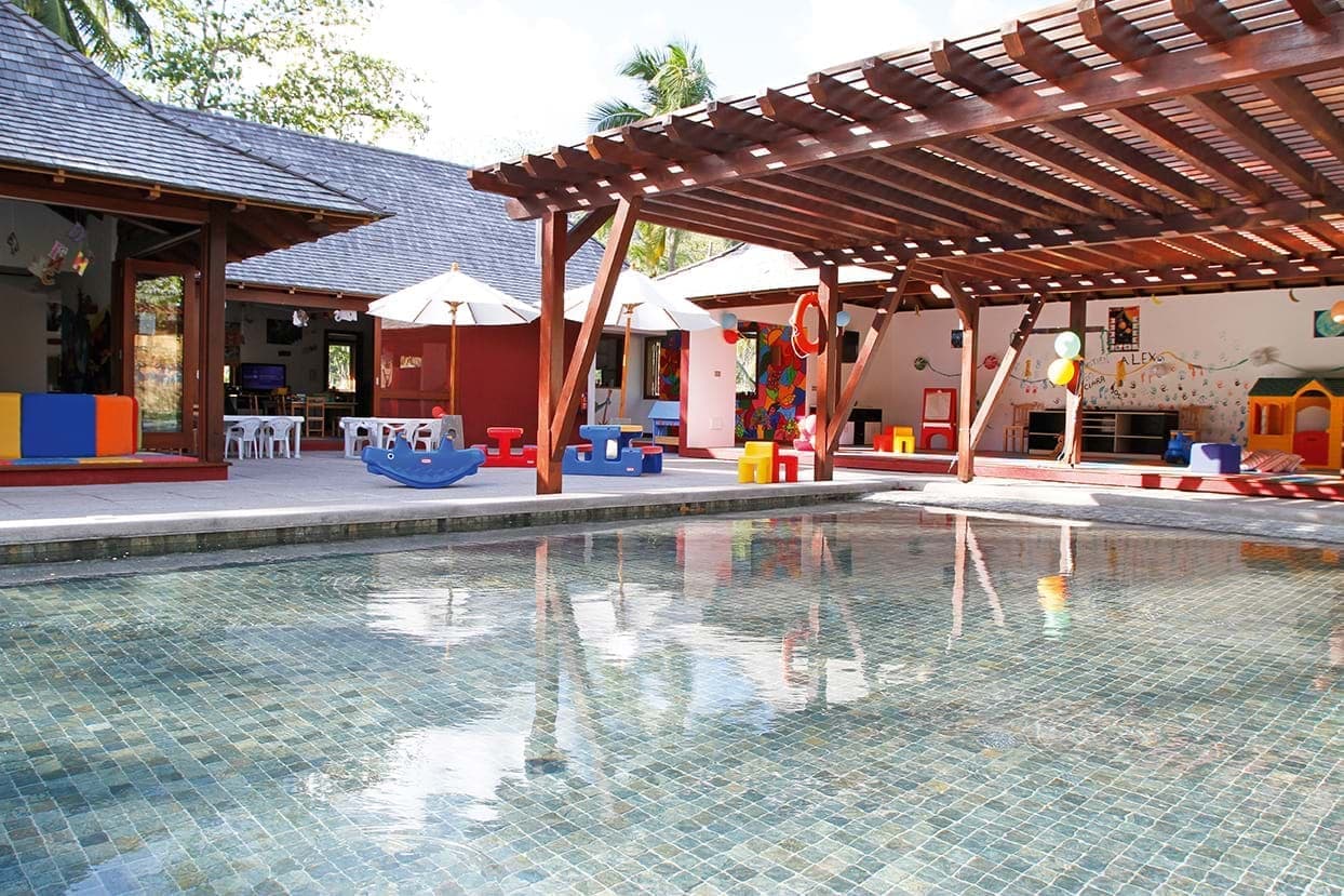 Shallow children's pool with colorful play equipment and wooden pergolas shading activity areas at Constance Ephelia resort.