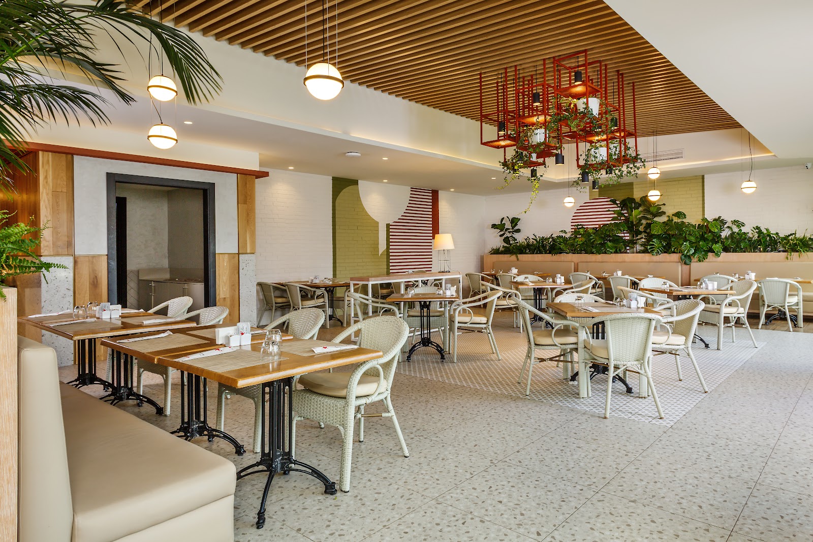 Modern dining room with wooden tables, woven chairs, hanging plants, and a slatted wood ceiling at Corendon Grand Park Lara.