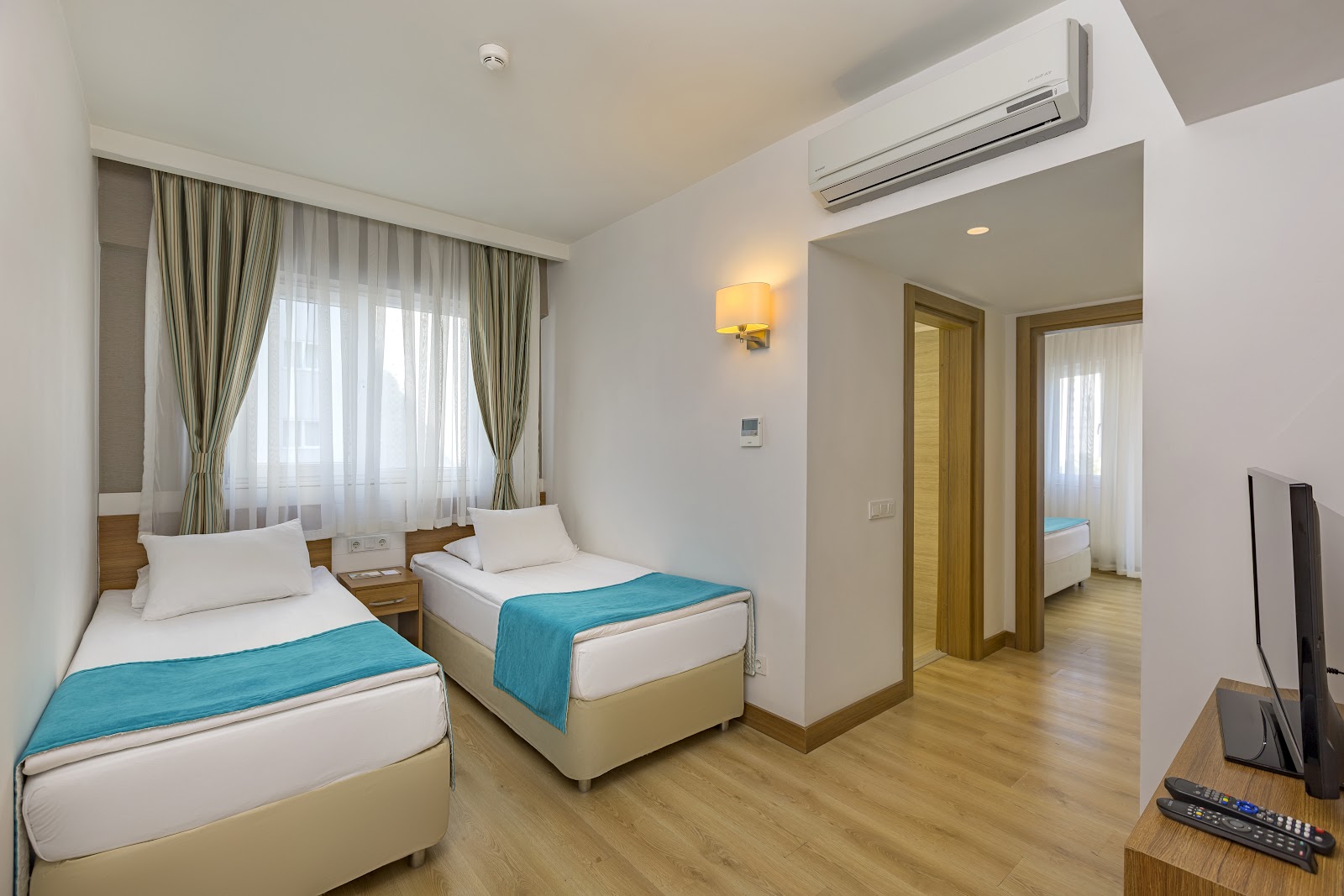 Twin beds with turquoise throws in a bright resort room with striped curtains, air conditioning, and wooden flooring.