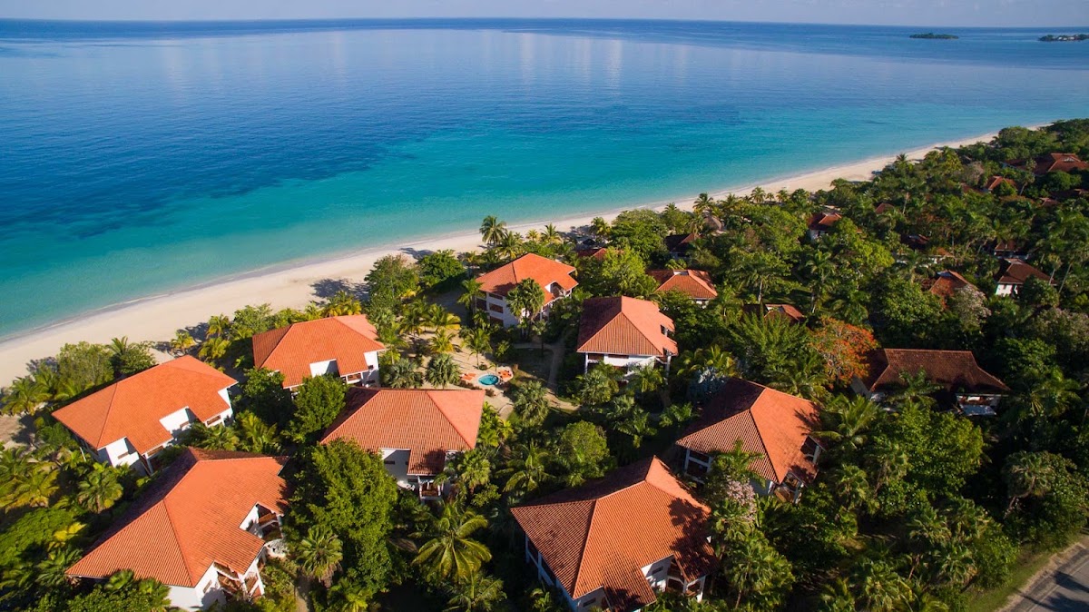 Aerial view of beachfront bungalows with orange roofs nestled in tropical vegetation along a turquoise lagoon.