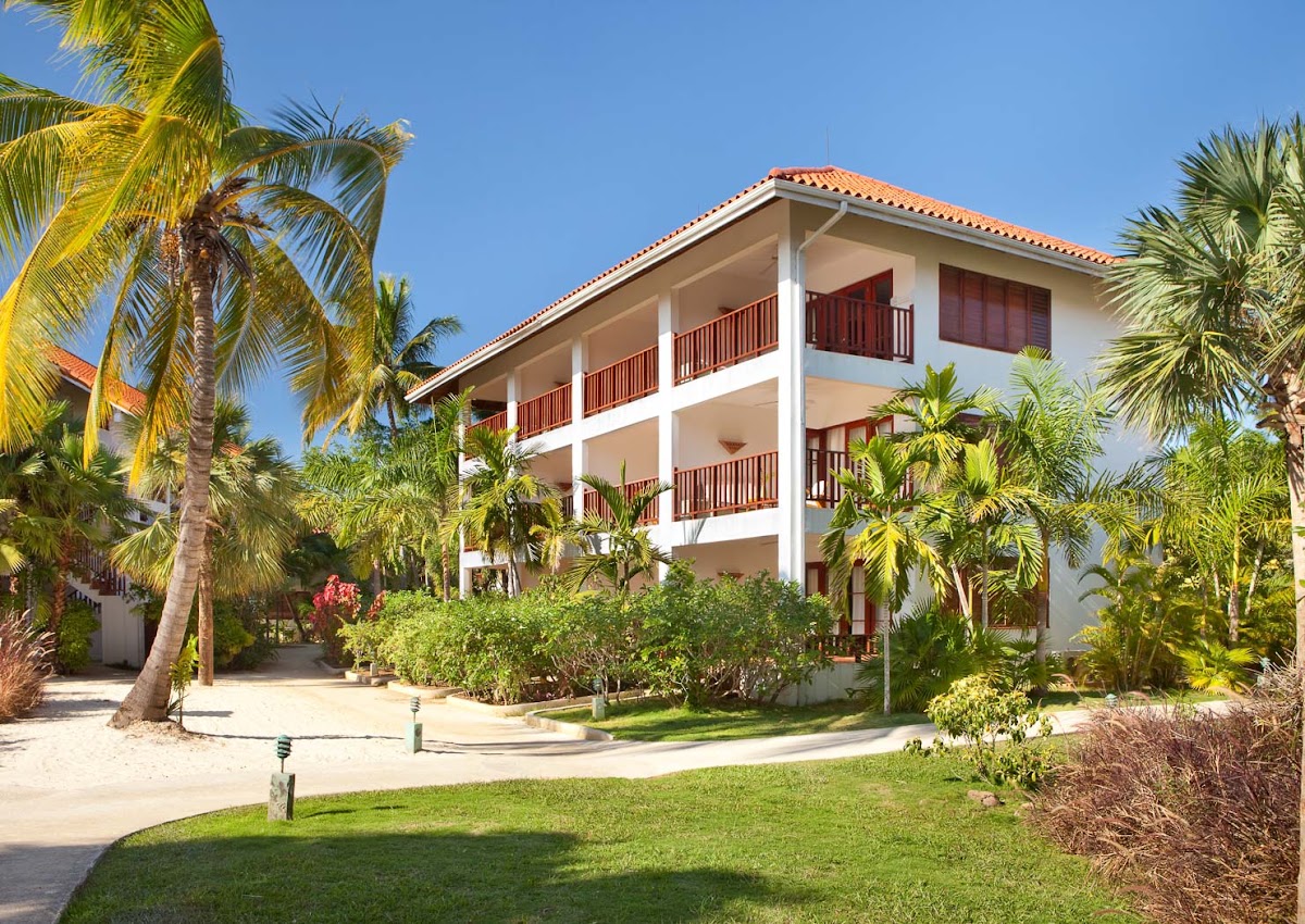 Three-story white building with terracotta roof and dark wood railings surrounded by palm trees and tropical landscaping at Couples Swept Away.
