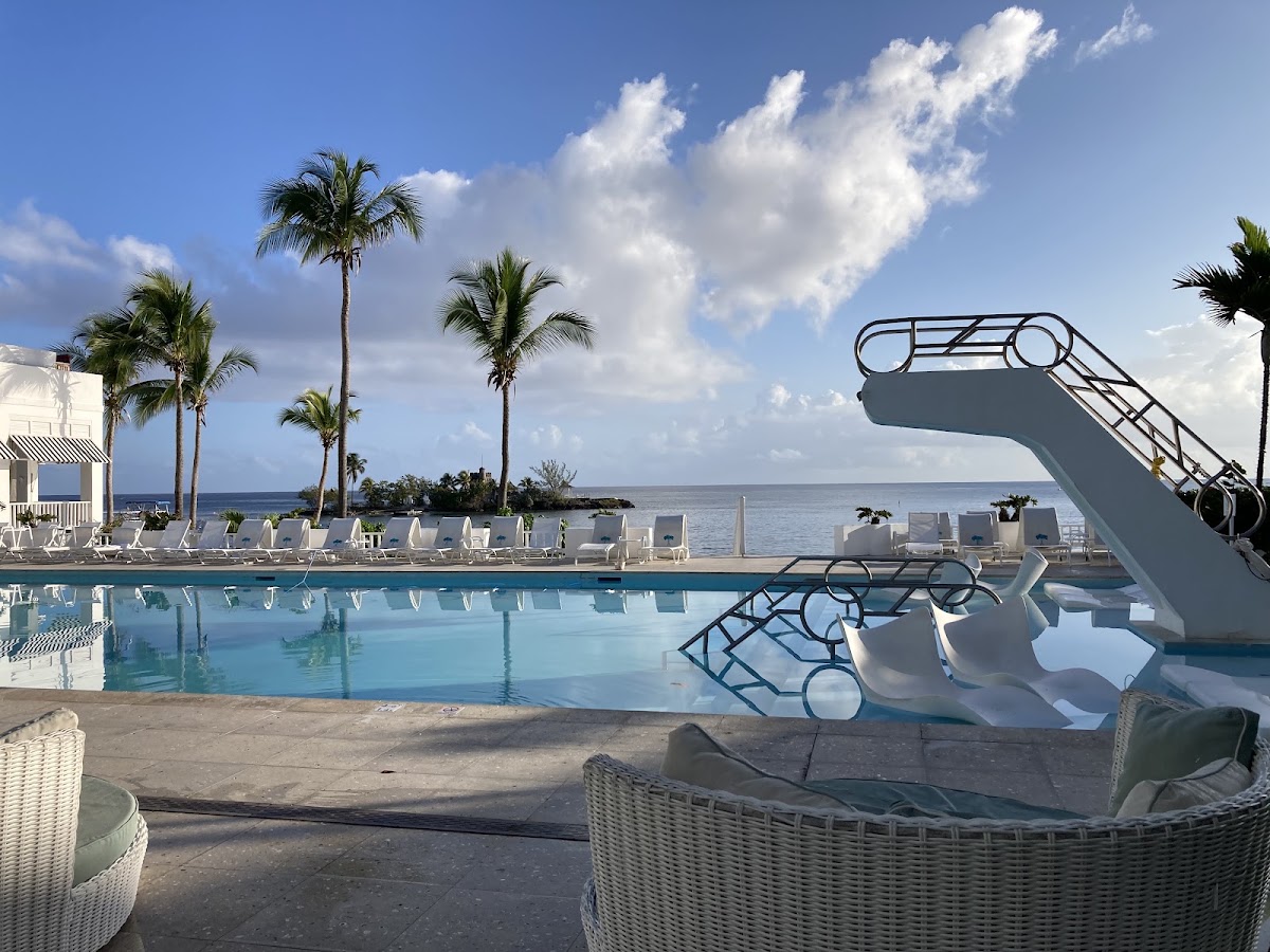 Poolside lounge chairs and a water slide overlook the turquoise pool and Caribbean Sea at Couples Tower Isle in Jamaica.