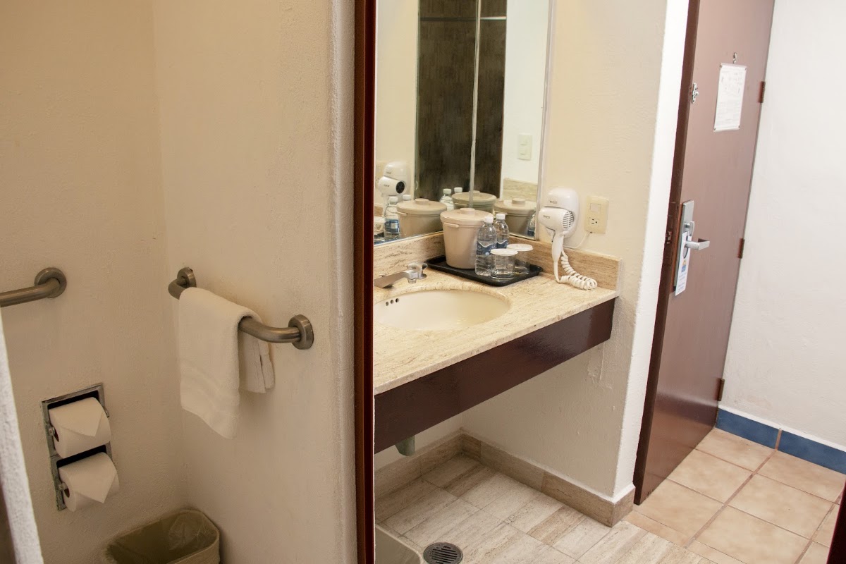 Hotel Cozumel & Resort bathroom with vanity counter, mirror, sink, and toiletries on travertine countertop.