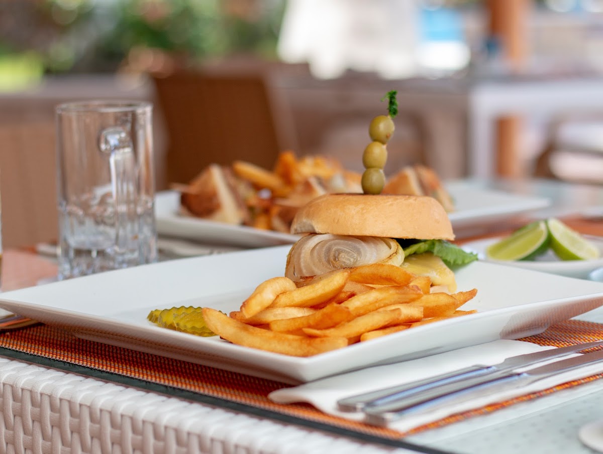 Plated sandwich with caramelized onions and olives served with fries at Hotel Cozumel & Resort's dining area.