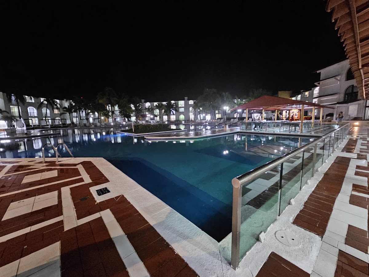 Illuminated pool at night with geometric tiled deck, metal railings, and resort buildings reflected in the water at Hotel Cozumel & Resort.