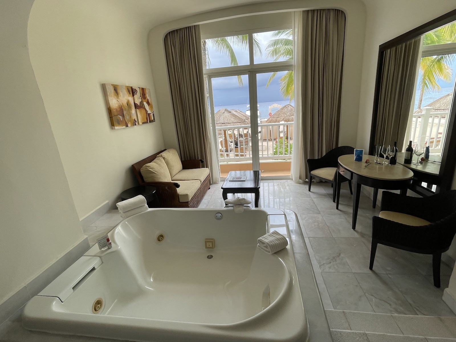 Bathroom at Cozumel Palace with marble double vanity, illuminated mirror, glass shower enclosure, and white towels.