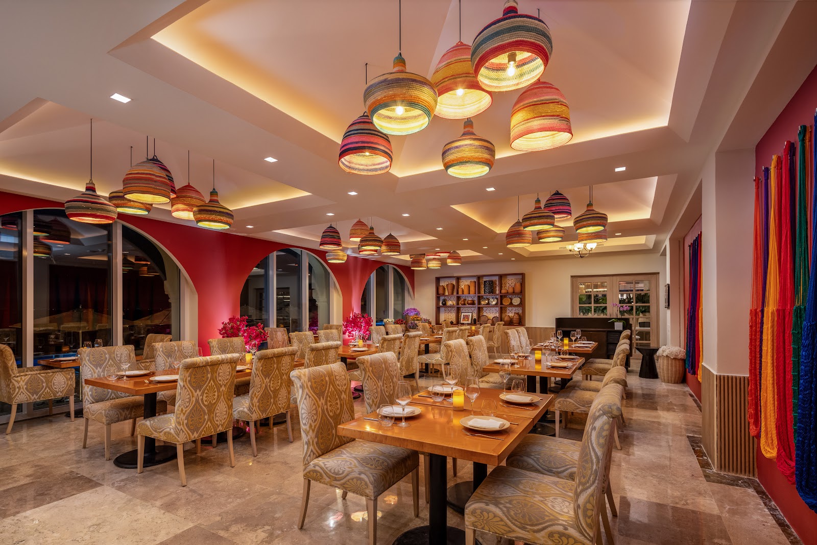 Cozumel Palace bar with navy cabinetry, white marble countertop, wooden bar stools, backlit shelving displaying bottles, and pendant lighting overhead.