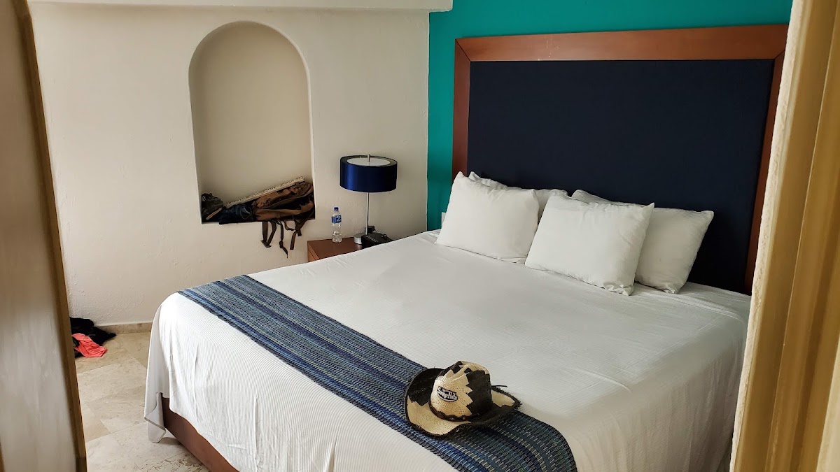Resort bedroom with queen bed, white pillows, blue stripe runner, dark headboard, teal accent wall, and bedside lamp.