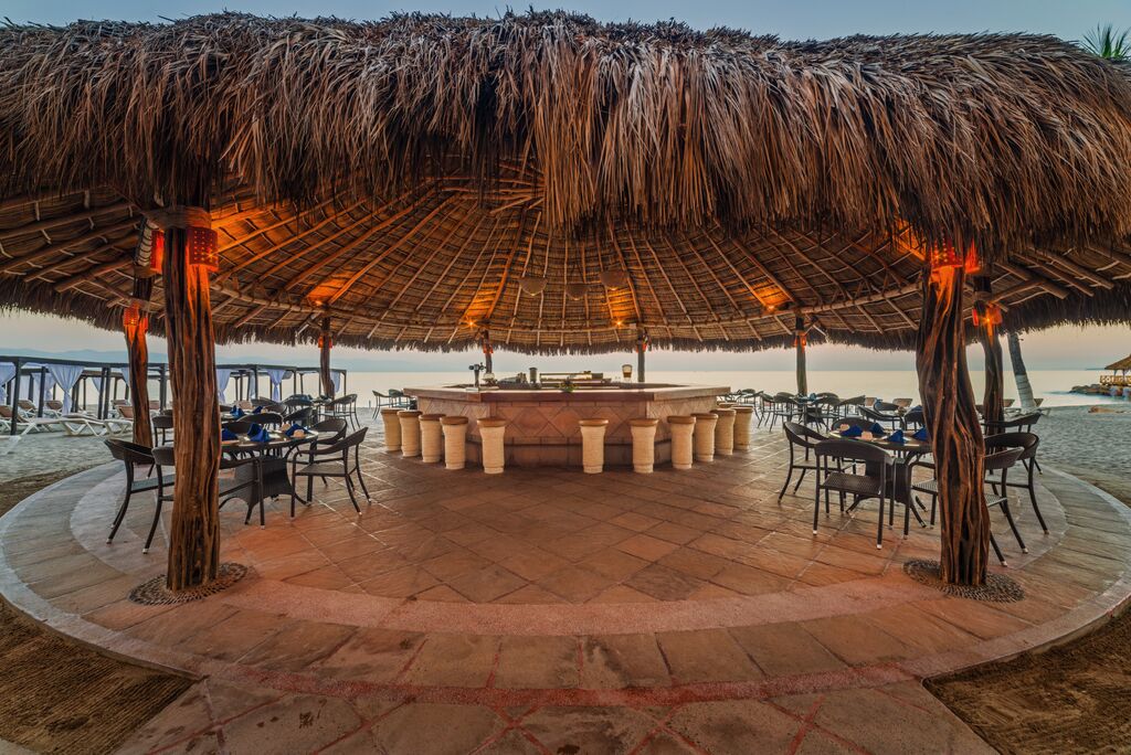 Beachfront bar with thatched palapa roof, terracotta columns, and seating overlooking the ocean at Crown Paradise Golden Resort Puerto Vallarta.