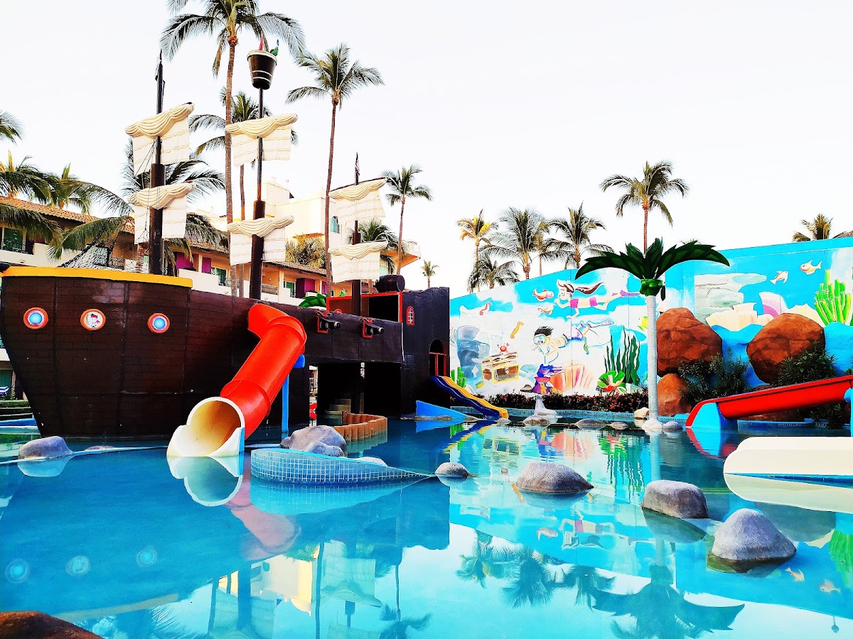 Pirate ship-themed kids pool with red slide, colorful underwater mural, and palm trees at Crown Paradise Golden Resort Puerto Vallarta.