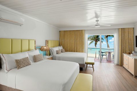Spacious hotel room at Crystal Cove with two beds, yellow headboards, and ocean view from the balcony overlooking palm trees.