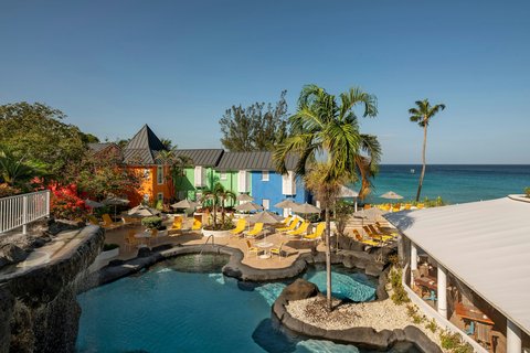 Crystal Cove's beachfront pool area features colorful cabanas, palm trees, and yellow loungers overlooking turquoise water and the Caribbean Sea.