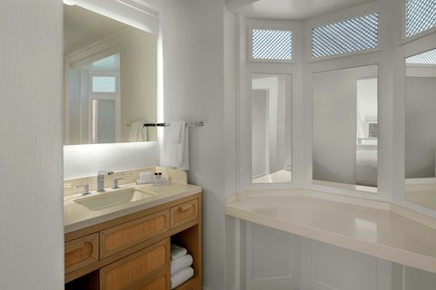 Bright bathroom at Crystal Cove with wooden vanity, illuminated mirror, and soaking tub by windows with louvered shutters.