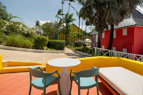 Turquoise chairs and white table on an orange terrace at Crystal Cove, with red bungalows and palm trees beyond.