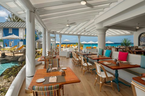 Beachfront dining pavilion at Crystal Cove with wooden tables, white chairs, and ocean views under white slatted roof.
