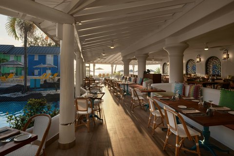 Covered dining pavilion at Crystal Cove with wooden tables, wicker chairs, and views of the pool and blue buildings beyond.