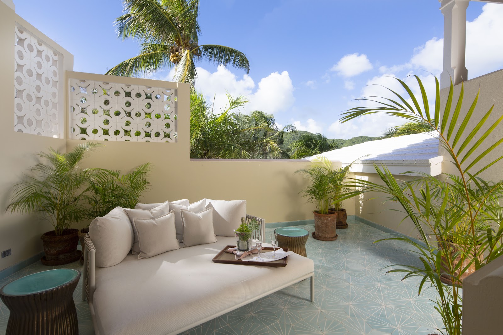 Private terrace at Curtain Bluff with cream sofa, potted palms, geometric screen wall, and hillside views under blue sky.