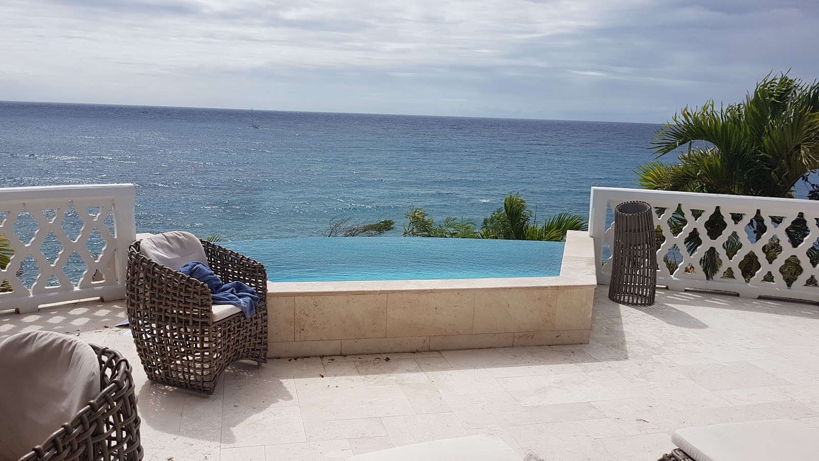 Woven lounge chairs on a terrace at Curtain Bluff overlook an infinity pool and calm turquoise ocean beyond.