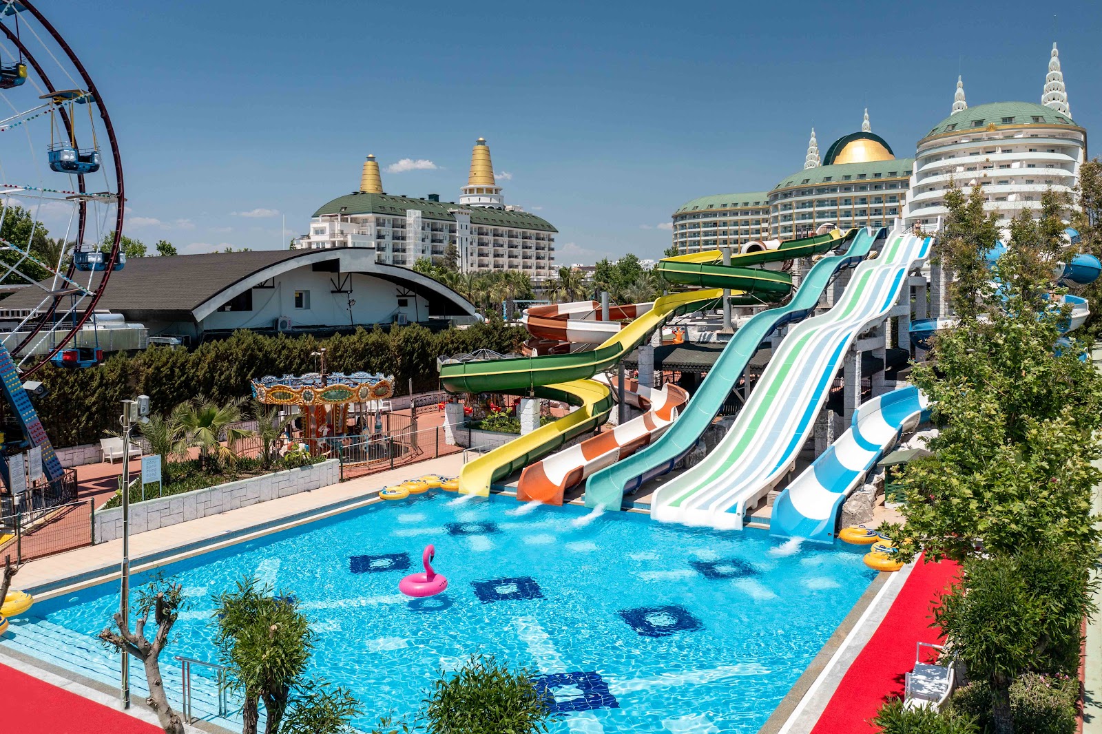 Water park with colorful slides and a bright blue pool at Delphin Imperial Hotel, distinctive tower buildings visible behind the recreational area.