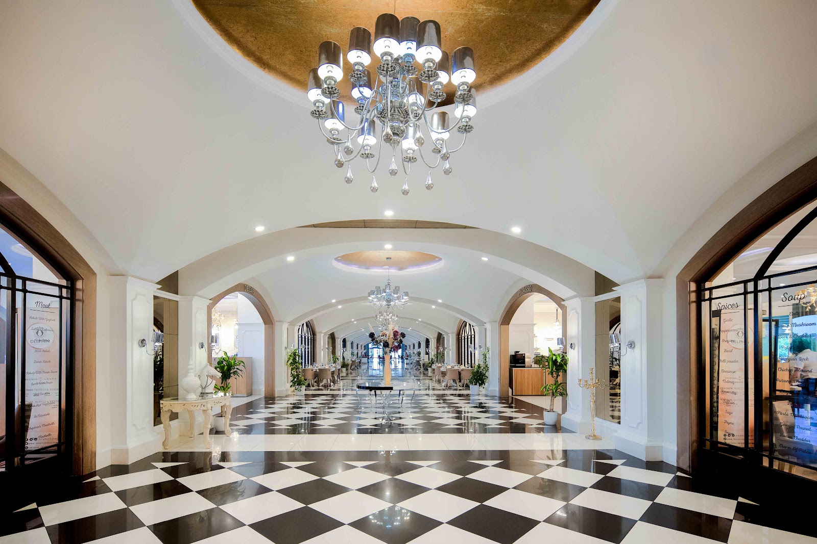 Modern buffet dining room at Delphin Imperial with arched ceilings, blue accent lighting, and multiple food stations along white and black counters.