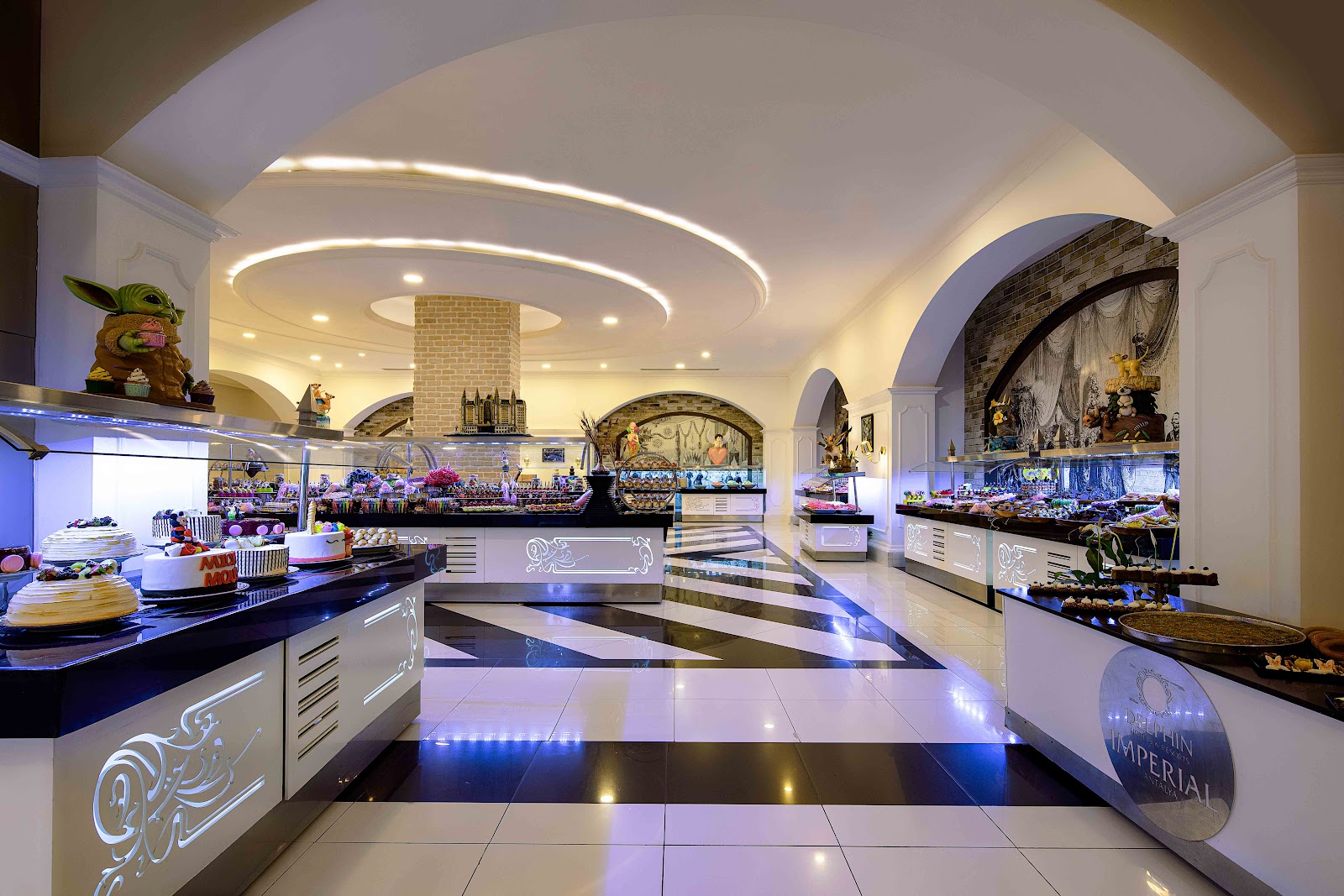 Elegant lobby corridor with black and white diamond-patterned marble floor, arched ceilings, crystal chandeliers, and archways leading to dining areas.