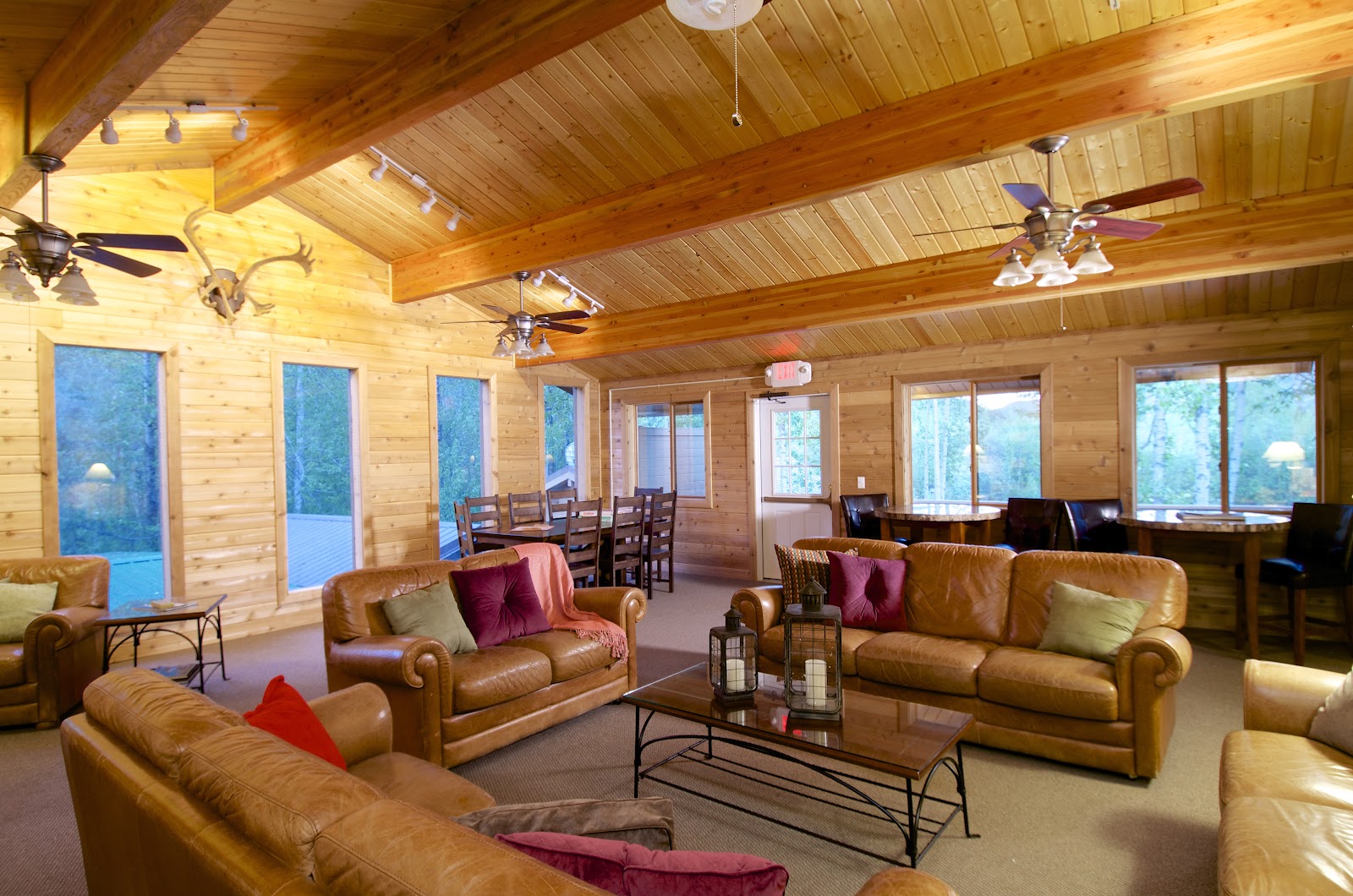Wooden cabins with wraparound porches sit beside a river with forested mountains rising behind them at Denali Backcountry Lodge.