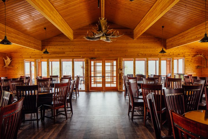 Spacious lodge interior with exposed wood beams, leather seating, and large windows overlooking forest at Denali Backcountry Lodge.