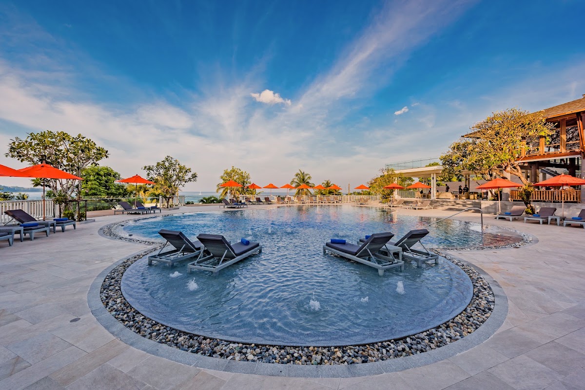 Circular pool with lounge chairs and ocean view under red umbrellas at Diamond Cliff Resort & Spa.