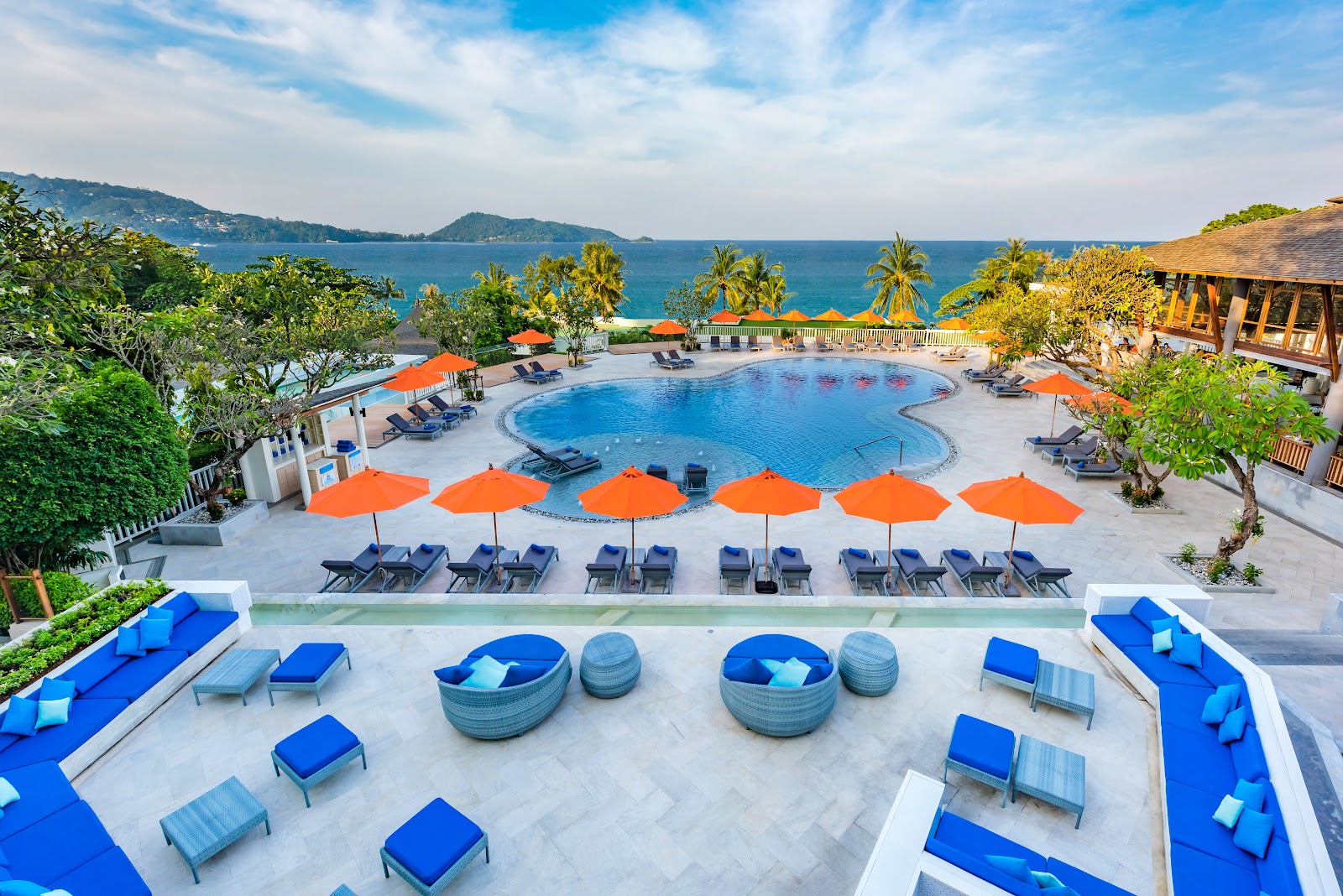 Aerial view of Diamond Cliff Resort & Spa pool area with orange umbrellas, loungers, and island views beyond palm trees and turquoise water.