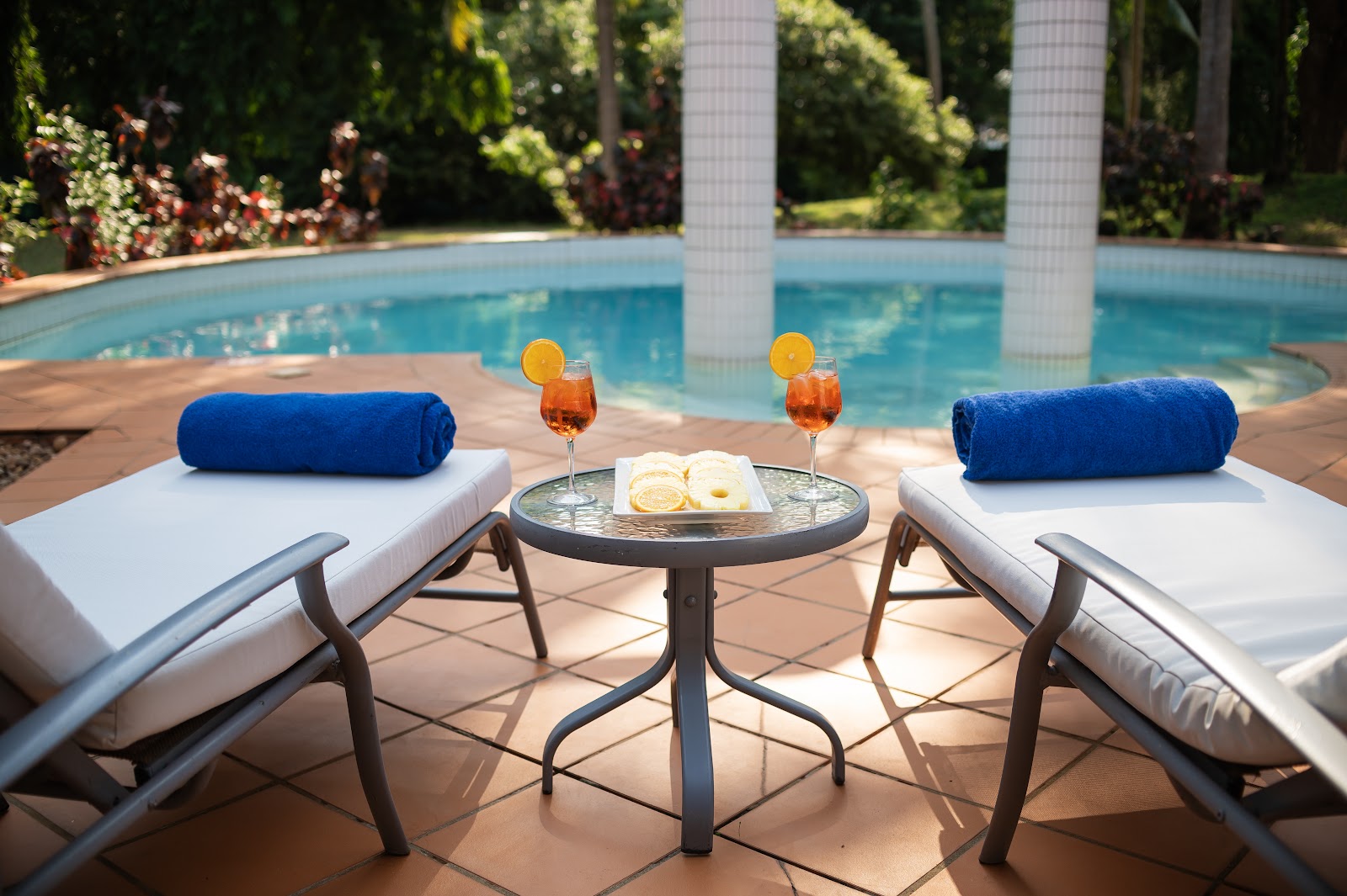 Two guests sit at the edge of a blue pool in front of white bungalows surrounded by tall palm trees at Diamonds Leisure Beach & Golf Resort.