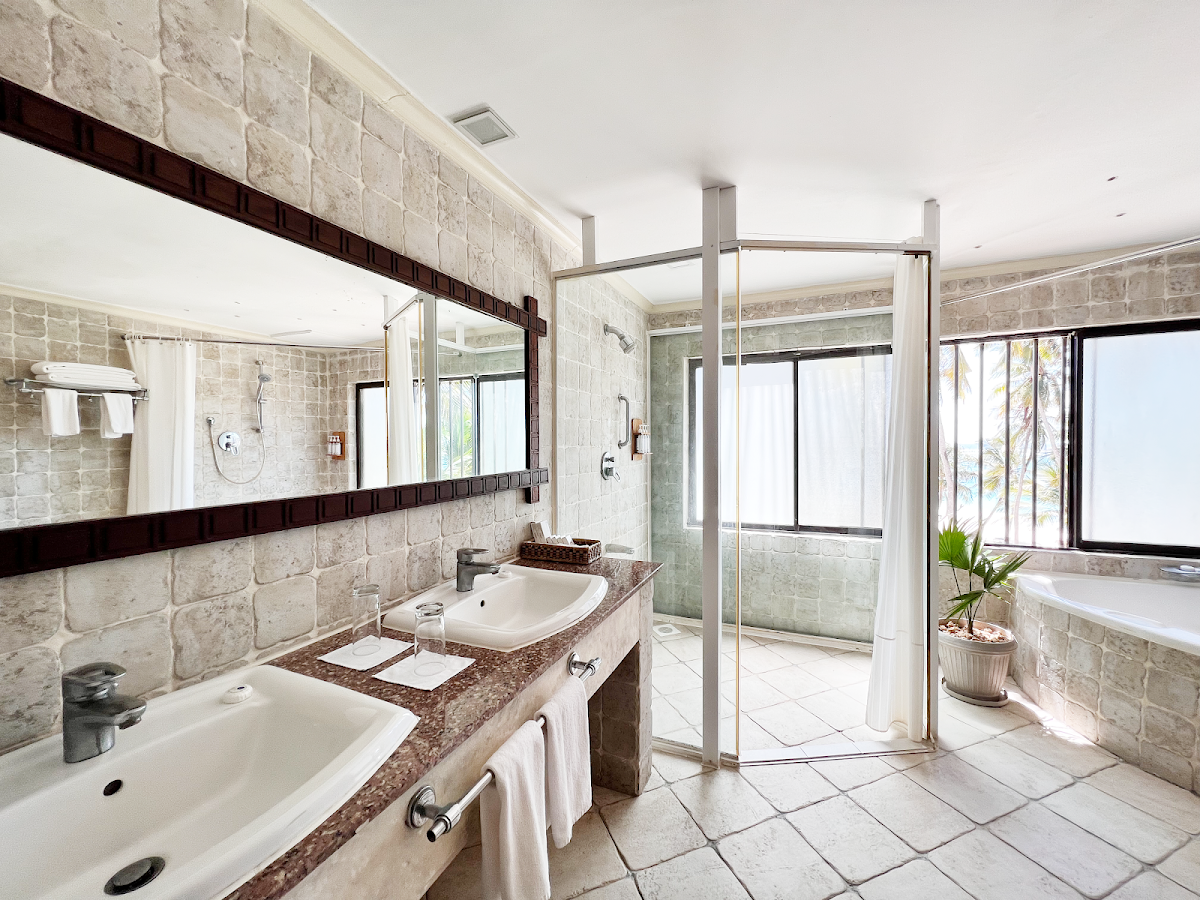 Spacious bathroom with dual sinks, granite countertop, stone tile walls, glass shower enclosure, and soaking tub at Diani Reef Beach Resort & Spa.