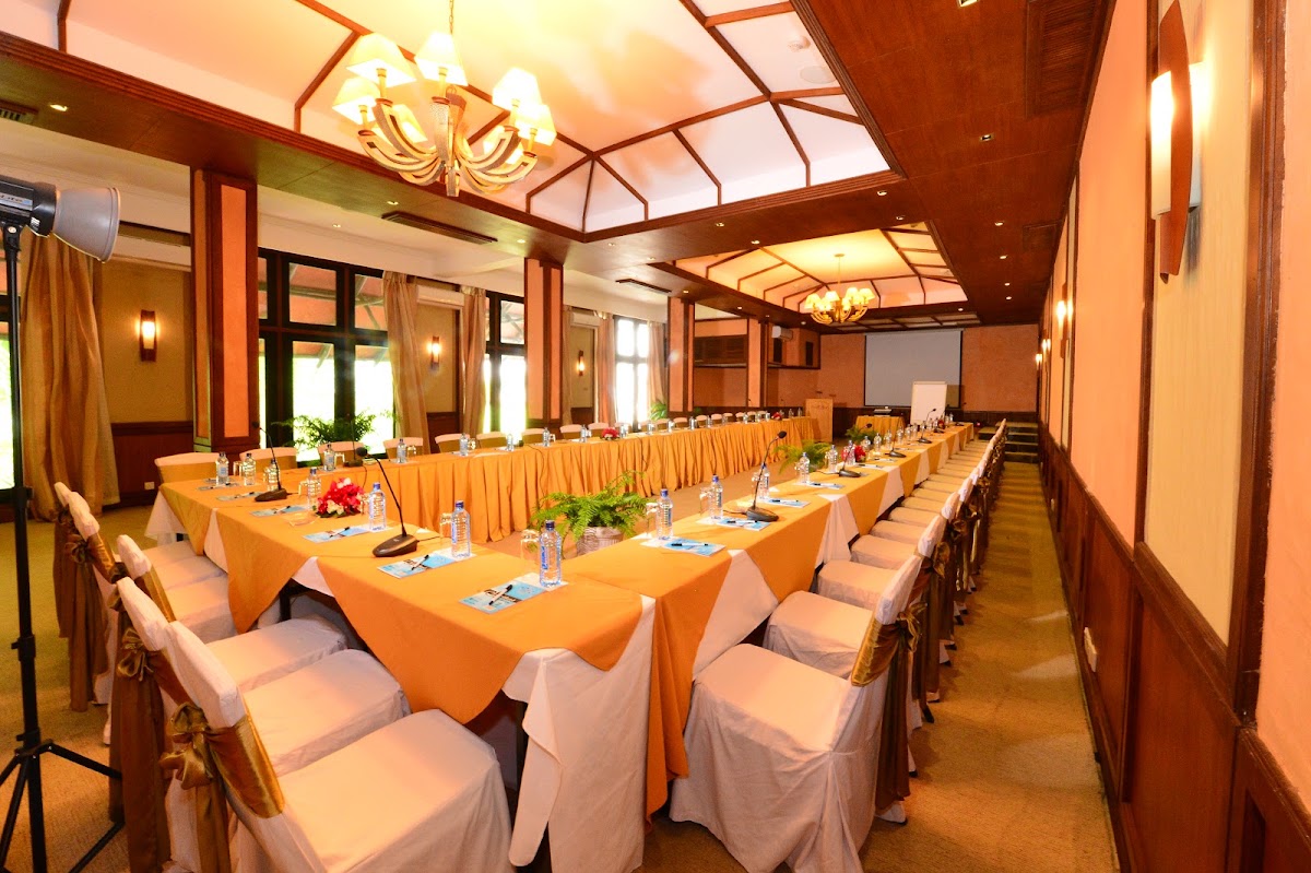 Long banquet hall with orange-draped tables and white chair covers arranged for a formal event, warm wood paneling and skylights overhead.