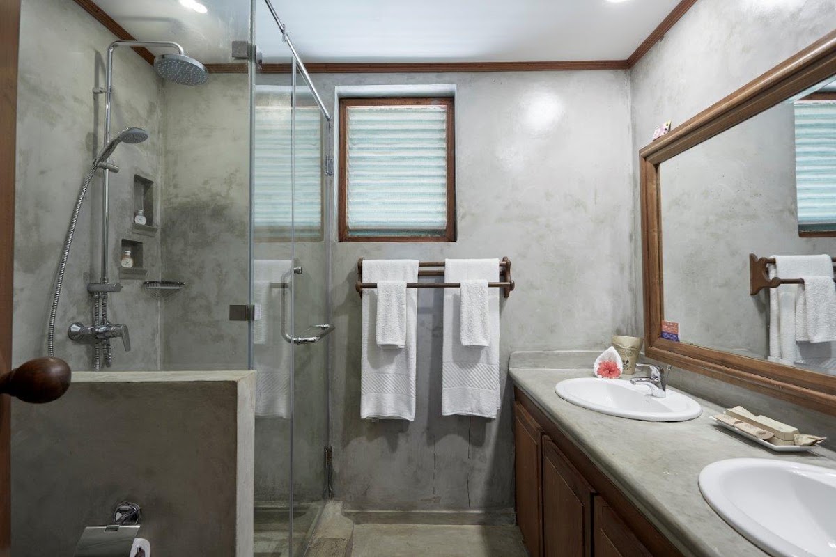 Modern bathroom with dual sinks, glass-enclosed shower, white towels on racks, and wood-framed mirror at Dickwella Resort and Spa.