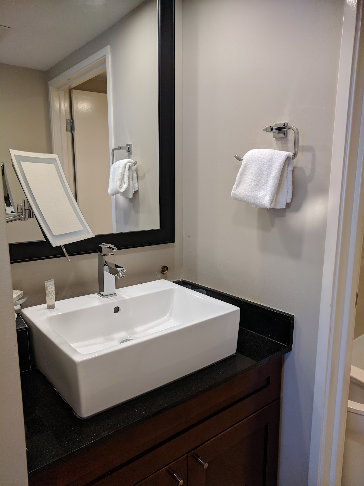 Bathroom vanity with rectangular white sink, black countertop, framed mirror, and white towels on chrome racks.