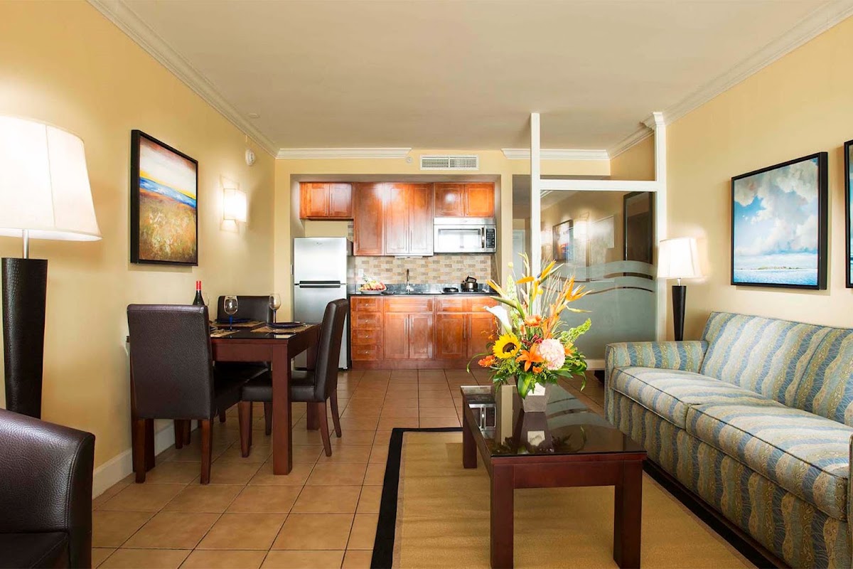 Resort suite with yellow walls, striped sofa, dining table, kitchenette with wood cabinets, and framed artwork at Divi Village Golf & Beach Resort.