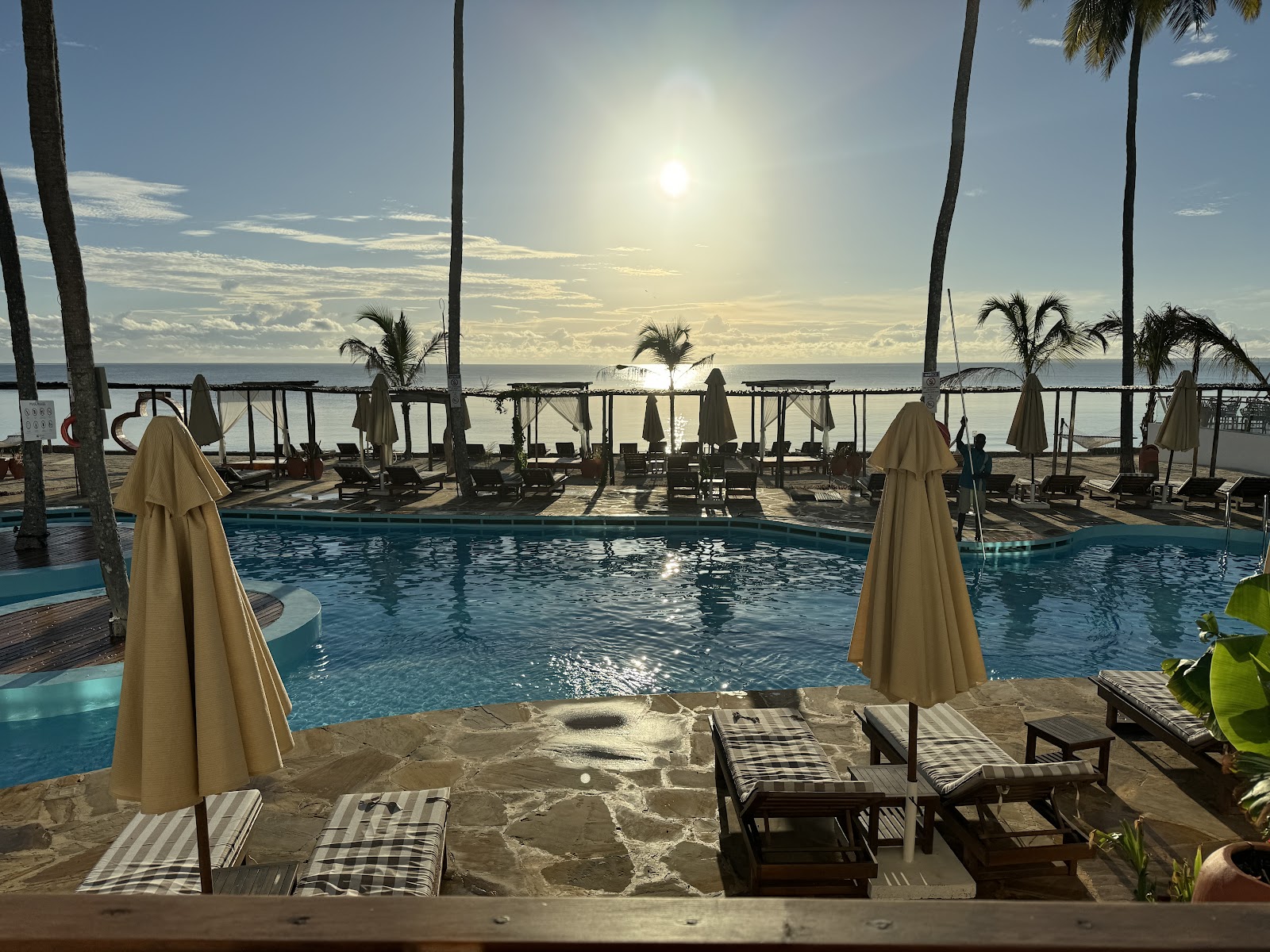 Curved blue pool with lounge chairs overlooking the ocean at Dream of Zanzibar Resort & Spa, palm trees dotting the beachfront terrace.