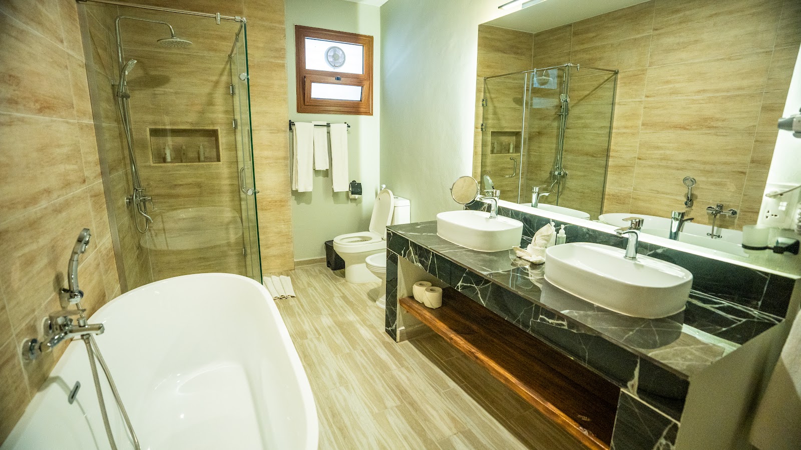 Spacious bathroom with freestanding soaking tub, dual vanities with white vessel sinks, glass-enclosed shower, and wood-look tile throughout.