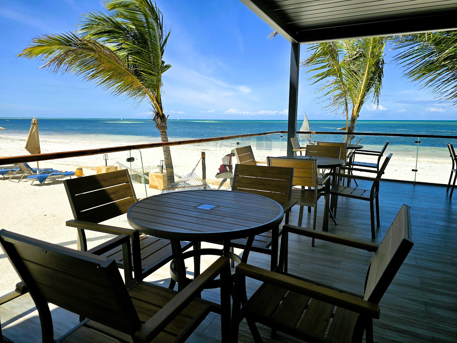 Beachfront dining deck at Dream of Zanzibar Resort & Spa with round tables, palm trees, and turquoise ocean beyond white sand.