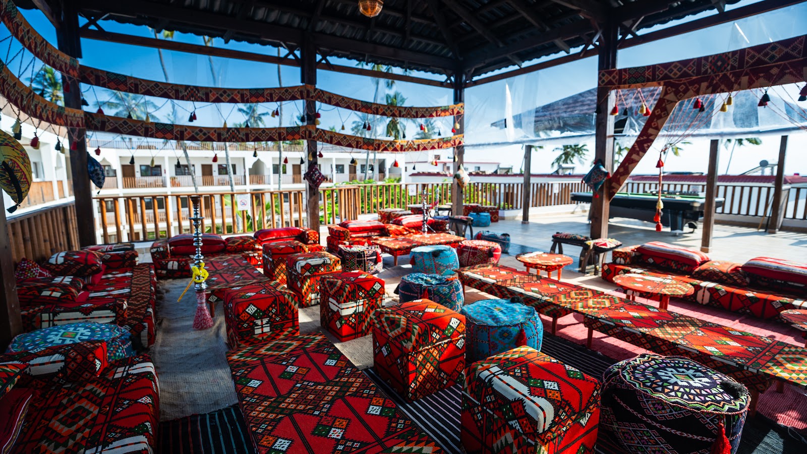 Bright lounge with cream and black seating, teal curtains, decorative masks on pale walls, and views to a boutique through tall windows at Dream of Zanzibar.