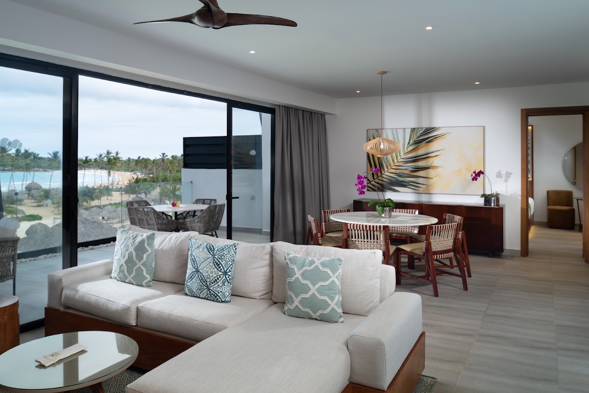Modern suite living area with cream sectional sofa, dining table, and ocean views through floor-to-ceiling windows at Dreams Macao Beach Punta Cana.