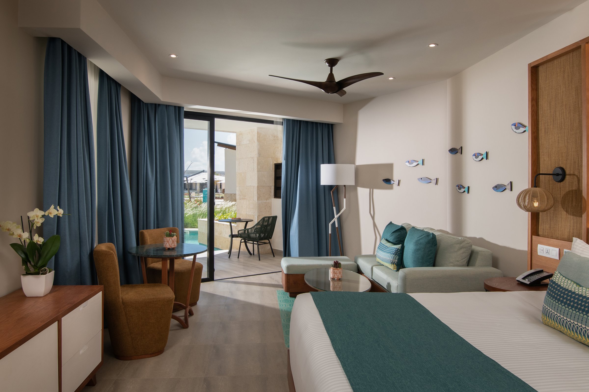 Junior suite king bed and sofa opening to a swim-up pool terrace.