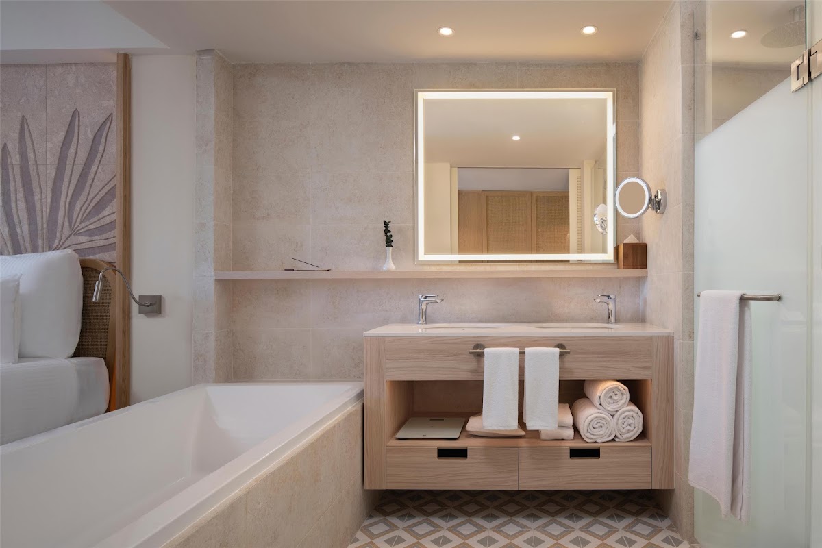 Modern bathroom with dual vanity, lit mirror, soaking tub, and rolled towels displayed on wooden shelving.